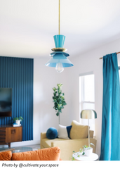 Teal Astro pendant light with brass hardware and sculptural stacked disc silhouette, a modern mid century inspired statement pendant hanging in a colorful living room with blue curtains and warm accent decor; bold design-forward ceiling light for eclectic interiors, maximalist homes, and retro modern styling that adds personality and a pop of color.