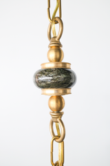 Close up detail of the green marble bead on a brass beaded pendant chain with decorative brass rings and hardware, highlighting the natural stone veining and vintage inspired metal accents, luxury artisan lighting detail for a one of one statement pendant, ideal keywords: green marble bead, brass pendant hardware, beaded chain pendant light, designer pendant lighting, custom lighting details