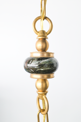 Close up detail of the green marble bead on a brass beaded pendant chain with decorative brass rings and hardware, highlighting the natural stone veining and vintage inspired metal accents, luxury artisan lighting detail for a one of one statement pendant, ideal keywords: green marble bead, brass pendant hardware, beaded chain pendant light, designer pendant lighting, custom lighting details