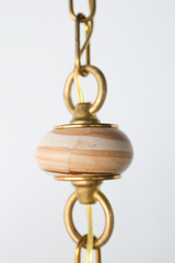 Closeup of teakwood spacer in unique one-of-a-kind pendant chained pendant - Close view of a cream sculptural pendant shade suspended from a brass beaded chain with terracotta sphere beads and light teakwood accent beads, a one of one hanging light with handmade looking jewelry style chain detailing, ideal for mid century modern lighting, grandmillennial decor, dopamine decor homes, and statement pendant lighting over a sink, island, or reading nook.