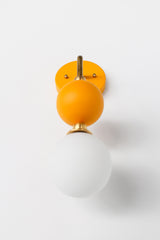 This mustard and brass sconce pairs a straight brass arm with a matte glass ball and a soft white opal glass globe at the bulb, giving it a warm, sculptural presence on the wall. It works well as a bedside light in place of a table lamp, beside a bathroom mirror, or anywhere a single statement sconce makes more sense than a matching pair.