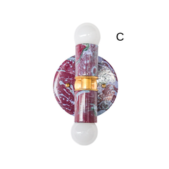A two-light wall sconce with a marbled finish blending black cherry, lilac, and green, joined by a brass center coupling. Two exposed globe bulbs sit above and below the fixture body. A statement piece for anyone building out a colorful bathroom or hallway instead of defaulting to plain brass or white.