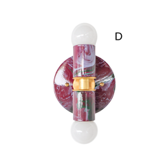Another angle on a two-light marbled wall sconce in black cherry, lilac, and green, showing the reverse side of the round backplate and brass hardware. Two exposed globe bulbs complete the fixture. A useful reference for seeing how the marbling shifts across the piece before choosing it for a bathroom or entryway.