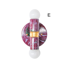 A closer look at a two-light wall sconce with a marbled finish in black cherry, lilac, and green, where the green streaking reads more prominently than in a full straight-on shot. Brass hardware joins the two arms, each holding an exposed globe bulb. Good for anyone searching for a colorful, non-boring sconce with real pattern and depth.