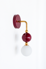 Another view of the black cherry and brass Ida sconce, with its brass gooseneck arm, saturated glass orb, and frosted globe bulb. A rich, sculptural option for a bathroom, hallway, or entry that wants color with real shape.