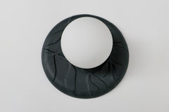 Matte black unglazed porcelain wall sconce with raised leafy relief and frosted glass globe, sculptural modern ceramic lighting