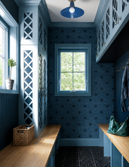 This mudroom commits to a single denim blue from the lattice-front cabinetry to the star-print wallpaper to the ceiling, with the Bruxelles Flushmount matching the color story exactly overhead in chrome. Wood bench tops and brass coat hooks warm up all that blue, while a woven basket, a wicker tote, and a small potted topiary keep the narrow space feeling functional and lived in rather than showroom-perfect.
