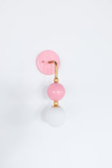 The Beaded Sconce in blush pink stacks a hooked brass arm, small brass ball joints, and a glossy pink powdercoated sphere above a soft white opal glass globe, giving the whole fixture a jewelry-like, beaded silhouette on the wall. It works well as a bedside light in place of a table lamp, beside a bathroom mirror, or anywhere a single statement sconce makes more sense than a matching pair.
