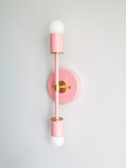 Blush pink Medium Thalia wall sconce with brass hardware, modern mid century inspired vertical double light with round backplate and two frosted globe bulbs, minimalist statement wall lighting for bathroom vanity, bedroom, hallway, powder room, or contemporary eclectic interiors