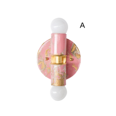 A hand-marbled Thalia wall sconce in a blush pink, cream, and gold colorway, shown against a clean light background to highlight its one-of-a-kind finish. This petite sculptural sconce features a round backplate, vertical center column, warm brass detailing, and globe bulbs for a playful yet polished look. The marbling gives it an artistic, custom feel that works beautifully in powder rooms, bathrooms, reading nooks, nursery spaces, and other small areas that need a soft pop of color. Ideal for lovers of do