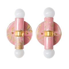 A pair of hand-marbled Thalia sconces in blush pink, cream, and gold is shown side by side, highlighting the natural variation in each individually marbled finish. Both fixtures feature a rounded backplate, globe bulbs, and brass detailing, but each one has its own distinct pattern, making them ideal for designers and homeowners who want lighting that feels custom and collected. These colorful wall sconces are perfect for flanking a bathroom mirror, brightening a powder room, or adding personality to a smal