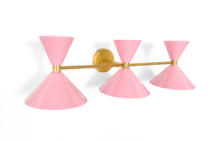 Head-on, the Triple Clancy shows off its rhythm: three glossy blush pink bowtie shades evenly spaced along a horizontal brass bar, anchored by a round brass backplate at the center. Each shade sends light up and down, making it as functional as it is pretty above a mirror. The blush-and-brass pairing is turning up in the most design-forward bathrooms right now, sweet enough to feel special, polished enough to feel timeless. Hang it above a double vanity or a wide powder room mirror for a symmetrical, statem