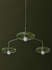 Studio-style detail of the Botanico chandelier against a dark green background, showing three translucent green botanical shades, white globe bulbs, and slim metal arms. The fixture feels sculptural, organic, and slightly whimsical, with a floral garden mood that works for maximalist interiors, artful dining rooms, feminine offices, botanical powder rooms, and anyone searching for a green chandelier, floral ceiling light, or nature-inspired statement fixture.