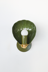 In deep olive, the Coquille Sconce trades sweetness for something earthier. The fluted shell shade, arm, and round backplate are color-drenched in glossy olive green powder coat, grounded by a cast brass rosette and ball detail beneath the exposed globe bulb. A grown-up green for English cottage bathrooms, moody powder rooms, coastal traditional spaces, and collected homes that want green lighting with depth instead of brightness.
