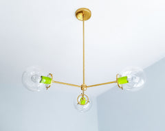 Bold chartreuse and brass lighting gives the Cadiz 3-light chandelier a playful contemporary edge. Designed by Sazerac Stitches, this customizable statement chandelier pairs three clear glass globes with vivid chartreuse accents and a streamlined branching brass frame. Its colorful modern design offers inspiration for eclectic dining rooms, creative kitchens, vibrant entryways, and interiors that mix saturated color with warm metallic finishes. Discover a distinctive globe chandelier made for expressive spa