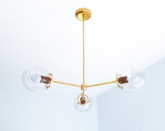Rich Fudge brown adds an earthy, grounded character to the Cadiz 3-light chandelier, a customizable statement fixture from Sazerac Stitches. The glossy brown powder-coated accents contrast with three transparent glass globes and a warm branching brass frame, creating sculptural lighting with an unexpected neutral palette. Consider it for brown dining-room ideas, warm contemporary kitchens, earthy bedrooms, or eclectic interiors layered with chocolate, caramel, cream, and brass. Explore modern globe lighting