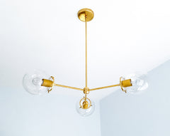Matte Mustard and brass give the Cadiz 3-light chandelier a warm, earthy color palette with a subtle retro influence. This customizable ceiling light by Sazerac Stitches pairs three clear glass globes with a slender branching brass frame and muted golden-yellow powder-coated accents. Its sculptural silhouette offers statement-lighting inspiration for ochre dining rooms, warm modern kitchens, eclectic entryways, and interiors combining mustard, olive green, rust, brown, or natural wood tones. Discover colorf