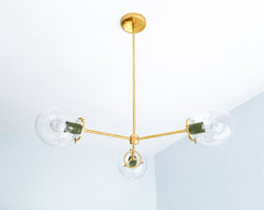 Olive Green and brass give the Cadiz 3-light chandelier a sophisticated, nature-inspired palette. Designed by Sazerac Stitches, this customizable ceiling fixture combines three clear glass globes, slender branching brass arms, and glossy green powder-coated accents. Its sculptural silhouette fits beautifully into botanical dining rooms, earthy kitchens, moody bedrooms, and eclectic interiors mixing olive, ochre, brown, cream, or warm wood tones. Discover distinctive globe lighting for layered, color-conscio