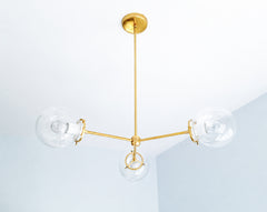 White and warm brass give the Cadiz 3-light chandelier a bright, versatile finish for neutral and colorful interiors alike. Designed by Sazerac Stitches, this customizable ceiling fixture pairs three clear glass globes with glossy White powder-coated accents and a slender branching brass frame. Its airy, sculptural design offers lighting inspiration for white kitchens, serene bedrooms, contemporary dining rooms, and elegant entryways layered in cream, pale blue, natural wood, or gold tones. Discover modern 