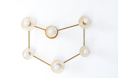 A Capricorn constellation wall sconce with six globe bulbs set in cream disc shades, each one a star, linked by thin raw brass rods that trace the sea goat sign. It reads like a star map on the wall and gives off a soft, scattered glow. Hang it over a bed, a sofa, or a crib in a Capricorn nursery. Cream and brass suit celestial decor, zodiac nursery ideas, and warm modern bedrooms, and it makes a thoughtful birthday gift for the Capricorn in your life.
