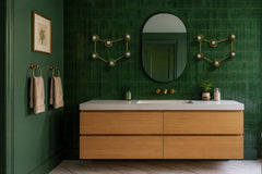 A pair of olive green and brass Capricorn constellation sconces flank an oval black mirror like two star charts on the wall. The bathroom is wrapped in glossy green vertical stack tile and deep green paint, with a floating warm wood vanity, a white quartz top, wall mounted brass faucet, brass towel rings, and a marble floor. Moody and earthy, it fits green bathroom ideas, modern organic design, and unique vanity lighting, with each light working as a wall sconce.