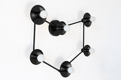 Black constellation wall sconce with six white globe bulbs set on round discs and joined by thin black rods in the shape of the Capricorn stars. From the side you can see how far each disc stands off the wall. Use it as a zodiac wall light over a bed or sofa, or as a flush mount ceiling light. Black against white reads like a drawing of a star chart and suits modern and minimalist rooms, retro space age lighting, and a celestial bedroom with other black metal.