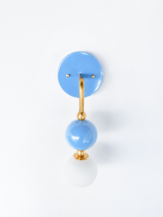 A single-arm wall sconce with a glossy sky-blue round backplate and a brass gooseneck arm that curves down to a matching blue glass orb, small brass ball accents, and a frosted globe bulb below. The stacked, sculptural shape brings softness and shape to a coastal bathroom, a nursery, or any room that wants gentle color with real presence.