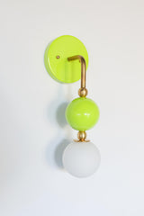 This side view shows off the full hooked silhouette of the Beaded Sconce in chartreuse, from the curved brass arm down through the glossy lime green glass ball to the soft white opal glass globe. The shape reads almost like a piece of jewelry on the wall, making it a strong choice for a bedside light, a bathroom vanity sconce, or anywhere a single statement fixture makes more sense than a matching pair.
