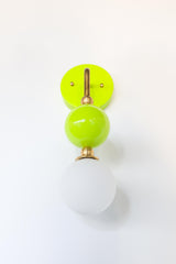 This straight-on view shows the full drop of the Beaded Sconce in chartreuse, from the hooked brass arm through a glossy lime green glass ball to the soft white opal glass globe below. The brass ring where the ball meets the globe adds a small, considered detail that keeps the whole fixture feeling finished rather than just functional. Works well as a bedside light, a bathroom vanity sconce, or anywhere a single statement fixture makes more sense than a pair.
