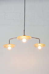 Close-up of a modern ceiling light fixture with three circular lampshades embedded with yellow pressed flowers & greenery, creating a bright and artistic design against a white background.