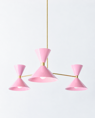 A sweet pink chandelier for a girl's bedroom, nursery, or any room that wants a little romance overhead. The Clancy Chandelier pairs three splayed brass arms with glossy blush-pink hourglass double-cone shades, each hung at a slightly different height for a relaxed, asymmetric silhouette. This pink reads flirty and cheerful without going saccharine, lovely against floral wallpaper, scalloped details, or crisp white millwork. A romantic color statement for grandmillennial, feminine traditional, or mid-centur