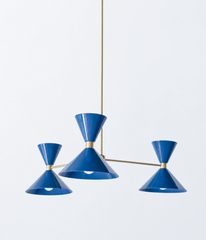 A saturated denim-blue chandelier for rooms that aren't afraid of color, a dining room, entryway, or study that wants a real focal point. The Clancy Chandelier pairs three splayed brass arms with glossy blue hourglass double-cone shades, each hung at a slightly different height for a relaxed, asymmetric silhouette. This deeper blue reads confident and graphic, striking against warm walls, patterned wallpaper, or old-house millwork. A fixture with conviction for bold and graphic, mid-century, or colorful tra