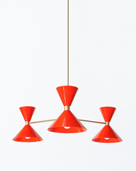 Bright flame orange and warm brass is the pairing that makes a room feel bold, sunny, and full of retro energy, and this mid-century modern Clancy chandelier brings them together beautifully. Three glossy red-orange double-cone shades radiate from a brass central hub on slim brass arms, in a fun, sculptural MCM silhouette that throws light up and down from each arm. The brass stem and collars warm up the punchy flame tone and give the whole piece a polished, collected feel. It's built to be the star over a 
