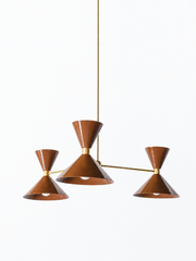 Rich chocolate brown and warm brass is the pairing that makes a room feel cozy, sultry, and a little seventies in the best way, and this mid-century modern Clancy chandelier brings them together beautifully. Three glossy fudge brown double-cone shades radiate from a brass central hub on slim brass arms, in a fun, sculptural MCM silhouette that throws light up and down from each arm. The brass stem and collars warm up the deep brown and give the whole piece a polished, collected feel. It's built to be the st