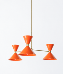 A knockout tangerine chandelier for anyone done playing it safe, a dining room, entryway, or kitchen that wants pure happy color overhead. The Clancy Chandelier pairs three splayed brass arms with glossy orange-peel hourglass double-cone shades, each hung at a slightly different height for a relaxed, asymmetric silhouette. This is joyful, high-energy color, striking against white walls, warm wood, or a wild wallpaper. A statement fixture for bold and graphic, maximalist, or mid-century rooms that refuse bei