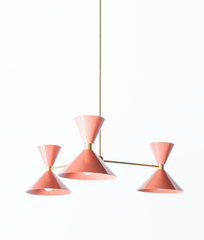 Soft peach and warm brass is the pairing that makes a room feel fresh, flirty, and a little sunny, and this mid-century modern Clancy chandelier brings them together beautifully. Three glossy peach double-cone shades radiate from a brass central hub on slim brass arms, in a fun, sculptural MCM silhouette that throws light up and down from each arm. The brass stem and collars warm up the coral-pink and give the whole piece a polished, collected feel. It's built to be the star over a dining table, a bedroom, 