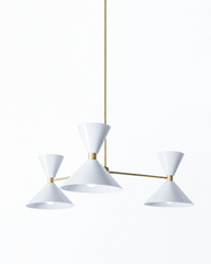 White and brass is the pairing that feels clean, timeless, and quietly polished, and this mid-century modern Clancy chandelier makes it sing. Three glossy white double-cone shades radiate from a brass central hub on slim brass arms, in a fun, sculptural MCM silhouette that throws light up and down from each arm. The warm brass stem and collars keep the crisp white from feeling cold and give the whole piece a collected, considered edge. It's built to be the star over a dining table, kitchen island, or entry,