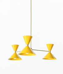 Bright yellow and warm brass is the pairing that makes a room feel sunny, confident, and full of retro personality, and this mid-century modern Clancy chandelier brings them together beautifully. Three glossy yellow double-cone shades radiate from a brass central hub on slim brass arms, in a fun, sculptural MCM silhouette that throws light up and down from each arm. The brass stem and collars warm up the punchy yellow and give the whole piece a polished, collected feel. It's built to be the star over a dini