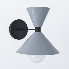 A cool slate-gray wall sconce with black hardware that brings quiet, tailored contrast to a powder room, hallway, or bedside. The Clancy Sconce carries the same sculptural double-cone shade as the Clancy chandelier, a wide cone below and a smaller cone flaring up above, here in glossy slate grey with a matching black collar, arm, and round backplate. The gray-on-black palette reads modern and a little industrial, calm against white trim, concrete, natural wood, or a moody wall. A restrained, versatile pick 