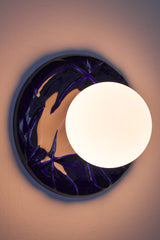 Installed cobalt Leafy Sconce with a warm glowing frosted globe and glossy cobalt leaf-relief backplate, creating a soft halo on the wall.