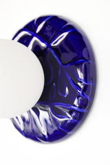 Angled view of cobalt blue ceramic wall sconce with frosted globe shade, Leafy Sconce sculptural leaf relief backplate, modern statement lighting for vanity or bedside.