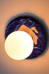 Installed cobalt Leafy Sconce with a warm glowing frosted globe and glossy cobalt leaf-relief backplate, creating a soft halo on the wall.