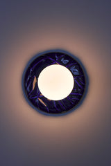 Cobalt blue Leafy ceramic wall sconce installed and turned on, frosted globe light with sculptural leaf backplate, modern bathroom vanity lighting with warm glow.