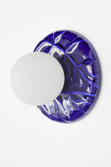 Cobalt blue ceramic wall sconce with frosted glass globe, Leafy Sconce in cobalt finish, installed and lit, modern bathroom vanity light with sculptural leaf texture.