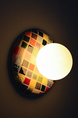 Colorful Cube Glazed Globe Sconce installed on wall and lit, handmade ceramic wall sconce with glossy multicolor cube grid glaze in reds, blues, greens, yellows, and neutrals, paired with a matte white glass globe shade, warm ambient light and soft glow, statement wall lighting for maximalist interiors, modern eclectic home decor, playful bedside sconces, bold hallway lighting, and colorful accent lighting for design forward spaces