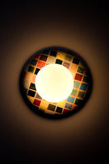 Colorful Cube Glazed Globe Sconce installed on wall and lit, handmade ceramic wall sconce with glossy multicolor cube grid glaze in reds, blues, greens, yellows, and neutrals, paired with a matte white glass globe shade, warm ambient light and soft glow, statement wall lighting for maximalist interiors, modern eclectic home decor, playful bedside sconces, bold hallway lighting, and colorful accent lighting for design forward spaces