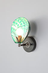 Hand-painted Coquille Sconce glowing with mermaid green ceramic shell, accented by layered white and navy brushstrokes; features black wall plate and silver-toned hardware with leaf detail, one-of-a-kind Art Deco wall light