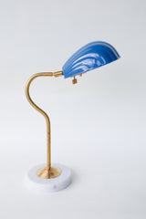 Coquille desk lamp in a muted Grey-Blue Denim color with a brass curved arm and solid marble base, featuring an Art Deco-inspired shell shade. This stylish midcentury modern lamp adds a coastal vibe and pop of color to any desk, bedside table, or reading nook, perfect for eclectic and contemporary decor styles.