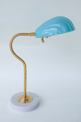 Coquille desk lamp in pastel sky blue with an elegant brass curved arm and a sturdy marble base, featuring a scalloped, Art Deco-inspired shell shade. This versatile midcentury modern lamp brings subtle sophistication and a touch of coastal charm to desks, bedside tables, or reading nooks, ideal for both minimalist and eclectic decor styles.