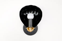 A black and gold wall sconce designed in a traditional chinoiserie-inspired style, featuring a shell-shaped black metal shade and an exposed round light bulb, mounted on an ornate gold base with intricate detailing.